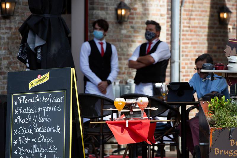 Two waiters, in protective face masks, wait on a nearly empty terrace at a restaurant in Bruges, Belgium. AP Photo