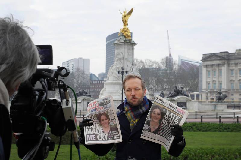 A television journalist holds up two British newspapers as he speaks to camera outside Buckingham Palace in London, Monday, March 8, 2021. Britain's royal family is absorbing the tremors from a sensational television interview by Prince Harry and the Duchess of Sussex, in which the couple said they encountered racist attitudes and a lack of support that drove Meghan to thoughts of suicide. (AP Photo/Kirsty Wigglesworth)