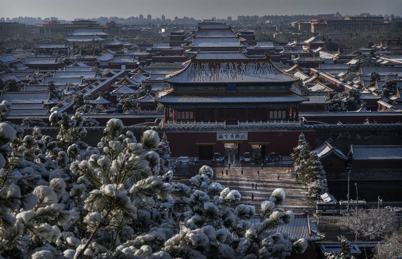 Snow on the rooftops as workers and security stand outside the Forbidden City before it opens the morning after a late spring snowfall on March 19, 2022 in Beijing. Getty Images