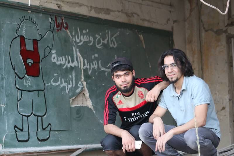 An image of Al Shami and Majd Mohadamani in 2014 in Daraya, in front of a mural in a ruined school.  Photo supplied by Abu Malek Al-Shami