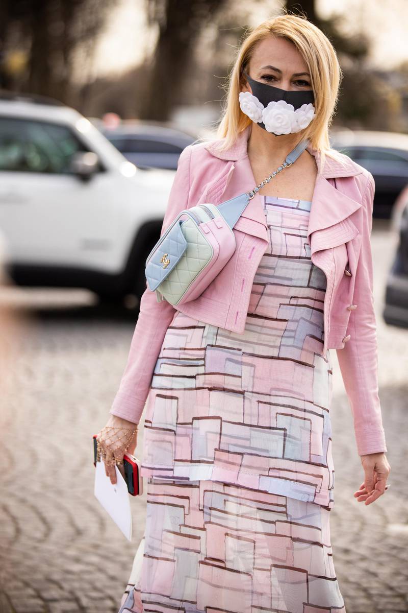 PARIS, FRANCE - MARCH 03: A guest wears a face mask with embroidered white flowers, a pale blue Chanel quilted bag, a pink jacket a flowing ruffled dress with printed geometric patterns, outside Chanel, during Paris Fashion Week - Womenswear Fall/Winter 2020/2021 on March 03, 2020 in Paris, France. Due to a sharp increase in the number of cases of coronavirus (COVID-19) declared in Paris and throughout France, several sporting, cultural and festive events have been postponed or canceled. The epidemic has exceeded 3200 dead for more than 92000 infections in sixty countries. To cope, the French government will requisition the stocks of protective masks by means of a decree published on Thursday. (Photo by Claudio Lavenia/Getty Images)