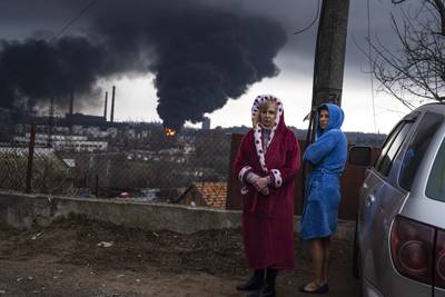 Women stand in their robes as smoke rises in the background after shelling in Odesa, Ukraine, on Sunday, April 3. AP