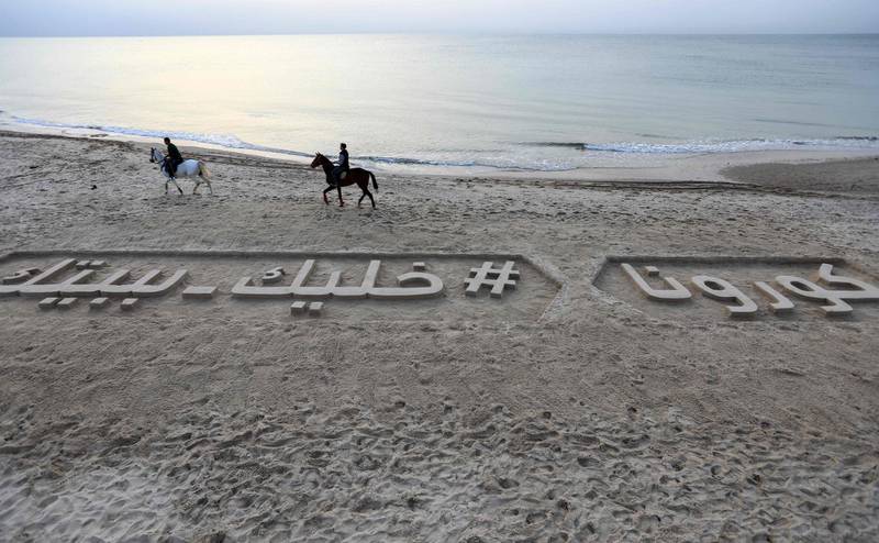 Horsemen ride past a sand sculpture along a beach in Gaza City, reading in Arabic "Corona #StayHome".   AFP