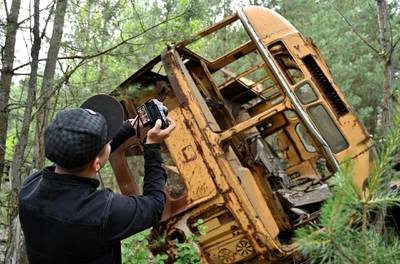 TOPSHOT - A visitor takes a picture at a wreckage of a bus in the ghost city of Pripyat during a tour in the Chernobyl exclusion zone on June 7, 2019. HBO’s hugely popular television series “Chernobyl” has renewed interest around the world on Ukraine’s 1986 nuclear disaster with authorities reporting a 30% increase of tourist demands to visit the affected area and tourist operators forecasting that number of tourists visiting the site may double this year up to 150.000 persons / AFP / Genya SAVILOV
