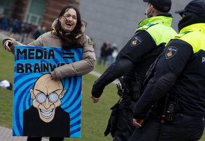 Dutch police talk to a demonstrator with a sign reading "Media = Brainwash" prior to breaking up a demonstration against coronavirus related government policies in Amsterdam, Netherlands. AP Photo
