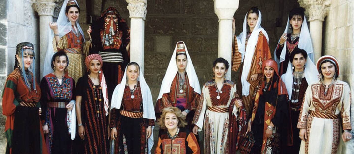 Maha Saca, the owner of the Palestine Heritage Center, at the center of women wearing regional clothing from all over Palestine.  Photo: Palestinian Heritage Center