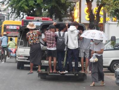 People hang off the back of a bus in Yangon, Myanmar. EPA