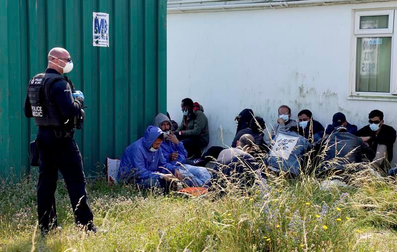 A police officer looks over a group of people sitting in the shade after being escorted from the beach by Border Force officers in Dungeness, southern England.