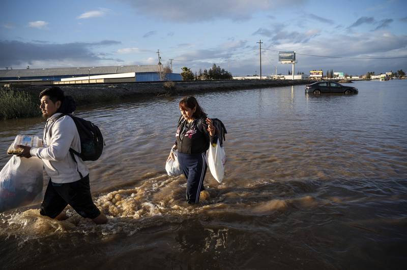 Angeles Molina carries belongings from her home flooded by the overflowing Bear Creek in Merced. AP