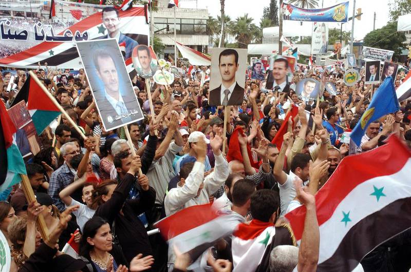 A handout picture made from the official Syrian Arab News Agency shows Syrian citizens holding the national flags and photos depicting President Bashar Assad as they gather to celebrate his victory in presidential elections, in Latakia province, Syria on 5 May 2014.  EPA/Sana handout