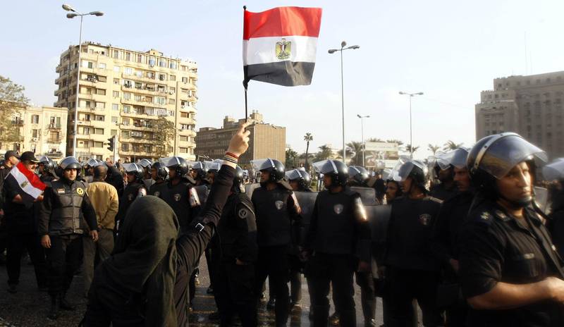 An Egyptian demonstrator holds up her national flag near Egyptian police during a protest in central Cairo to demand the ouster of President Hosni Mubarak and calling for reforms on January 25, 2011. The protesters, carrying flags and chanting slogans against the government, rallied in a protest inspired by the uprising in Tunisia which led to the ouster of Zine El Abidine Ben Ali.  AFP PHOTO/MOHAMMED ABED / AFP PHOTO / MOHAMMED ABED