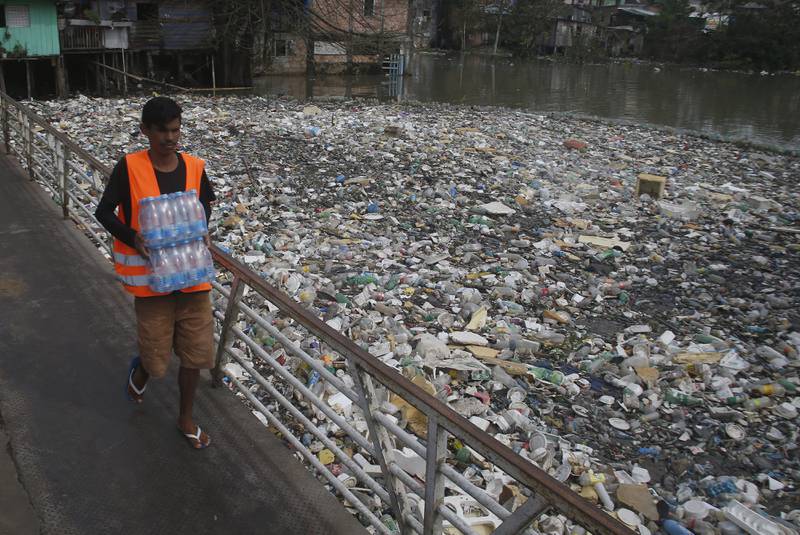 A man carries water bottles across the heavily polluted Negro River in Manaus, Brazil. About 35 tonnes of rubbish are removed daily from the river. AP
