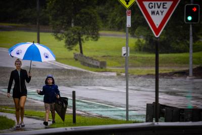 Residents walk past a flooded creek in the Cannon Hill suburb of Brisbane. AFP