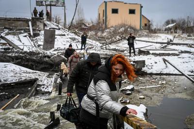 Civilians cross a river on a blown-up bridge on Kyiv's northern front. Defending the capital is a 'key priority', Ukraine's president has said. AFP