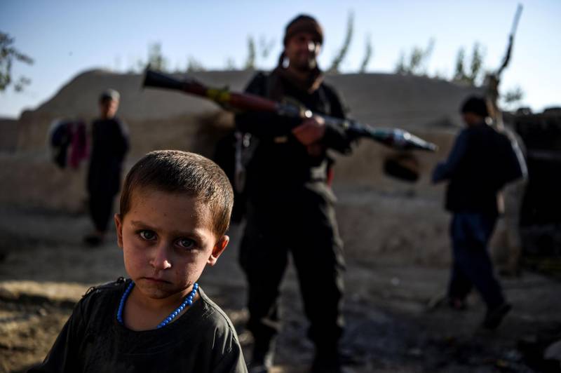 A young boy looks at the camera as a policeman holding a rocket-propelled grenade (RPG) stands behind in a house at Deh Qubad village in Maiwand district of Kandahar province, Afghanistan. AFP