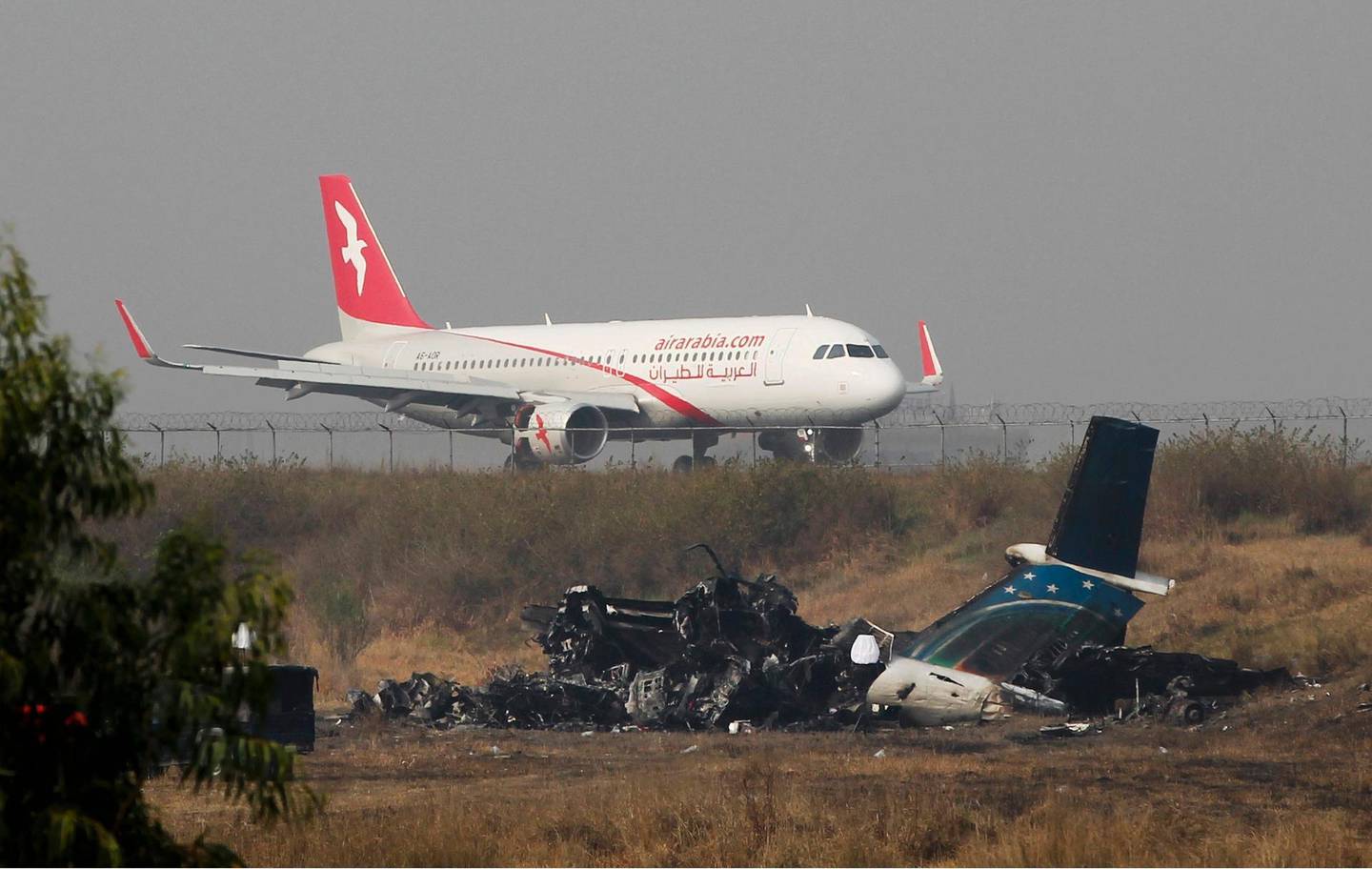 Remains of Bangladesh's US-Bangla Flight BS211 lies on the ground as a plane takes off from Tribhuvan International Airport in Kathmandu, Nepal, Tuesday, March 13, 2018. The plane, which was coming from Bangladesh, was flying low and erratically before striking the ground and erupting in flames on Monday. US-Bangla Airlines Flight BS211 from Dhaka to Kathmandu was carrying 67 passengers and four crew members. (AP Photo/Niranjan Shrestha)