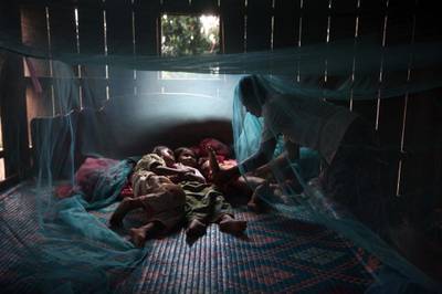 FOR MALARIA / SMALPOX GALLERY. PREY MONG KOL, CAMBODIA - JULY 18:  Yonta ,6, rests with her sister Montra,3, and brother  Leakhena, 4months under a mosquito bed net keeping dry from the monsoon rain July 18, 2010 in Prey Mong kol village in Pailin province. Part of the great success of controlling the malaria is due to the distribution by National Malaria center (CNM)  and WHO of the long lasting mosquito nets that also contain the insecticide embedded into the net causing the insect to die upon contact. According to WHO,  around 3,000 people from various villages have been tested so far in an area where resistance to artemisinin surfaced, which is the most effective ingredient vital to all anti-malarial drugs used throughout the world, especially in fighting the more lethal Falciparum malaria. The results are proving that the resistant malaria has almost disappeared from the area. (Photo by Paula Bronstein/Getty Images)