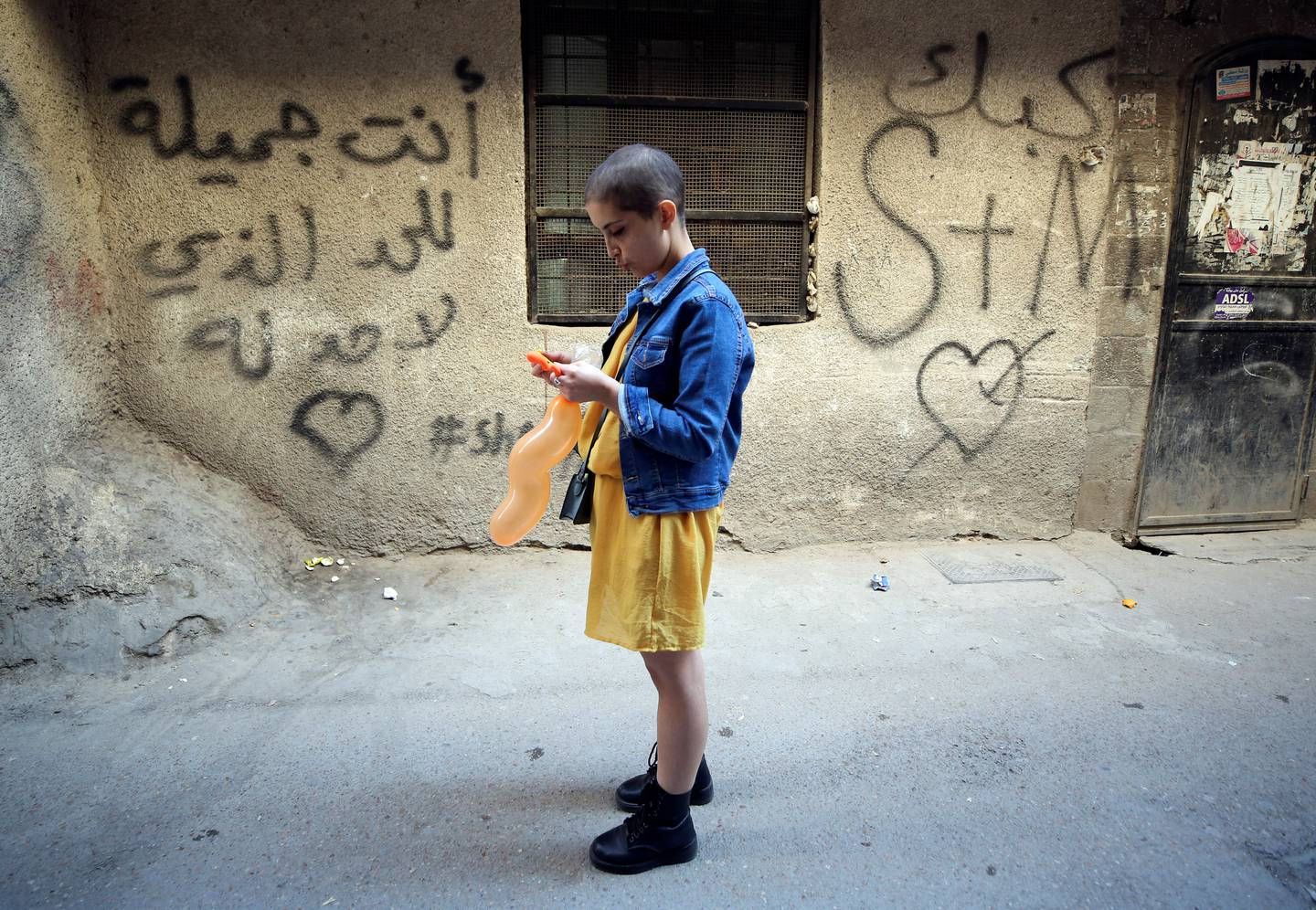 Rawan Tarabih, a 29 year-old cancer patient, uses her phone near a writing on a wall that reads " You are indefinitely beautiful" during a photoshoot in Damascus, Syria, November 10, 2021.  Picture taken November 10, 2021.  REUTERS / Yamam al Shaar