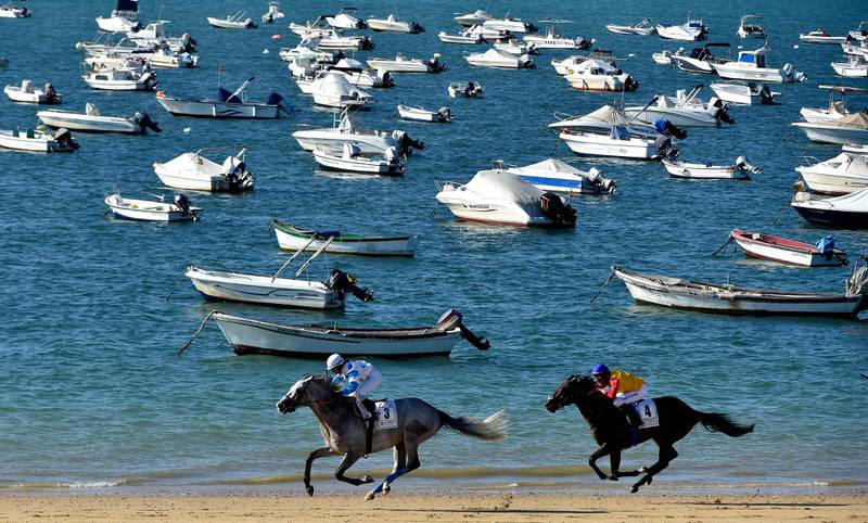 Jockeys race along a beach during the annual beach horse races in Sanlucar de Barrameda near Cadiz on August 25, 2022.  - While originally the horse races on the beach of Sanlucar de Barrameda were informal competitions of horse owners who used them for fish transport from the old port to the local markets and nearby towns, the first official race organized by the Royal Horse Races Society of Sanlucar was celebrated on August 31, 1845.  (Photo by CRISTINA QUICLER  /  AFP)