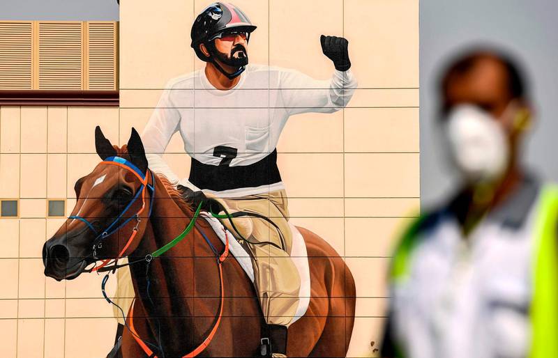 A mask-clad worker walks near a mural depicting Dubai Ruler Sheikh Mohammed bin Rashid riding a horse as a jockey, along Al Mustaqbal Street in Dubai.  AFP