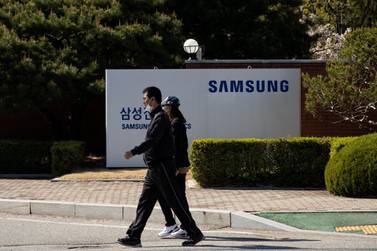 People wearing protective masks walk past the Samsung signage at the company's mobile factory in South Korea. Bloomberg