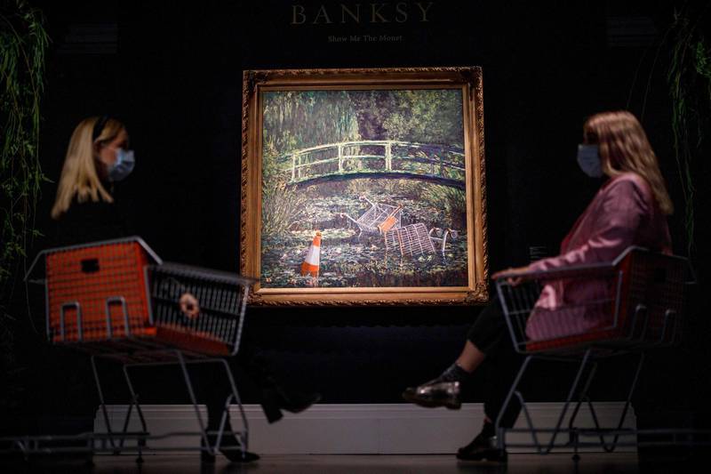 Assistants pose by an artwork entitled Show me the Monet by Banksy at Sotheby's Galleries in London in October 2020. AFP