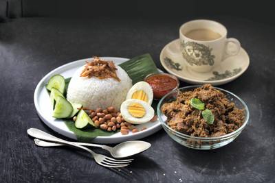 Nasi lemak (Malay fragrant rice dish cooked in coconut milk and pandan leaf) on rustic wooden table top along side with recipe ingredient. Flat lay image with negative space.