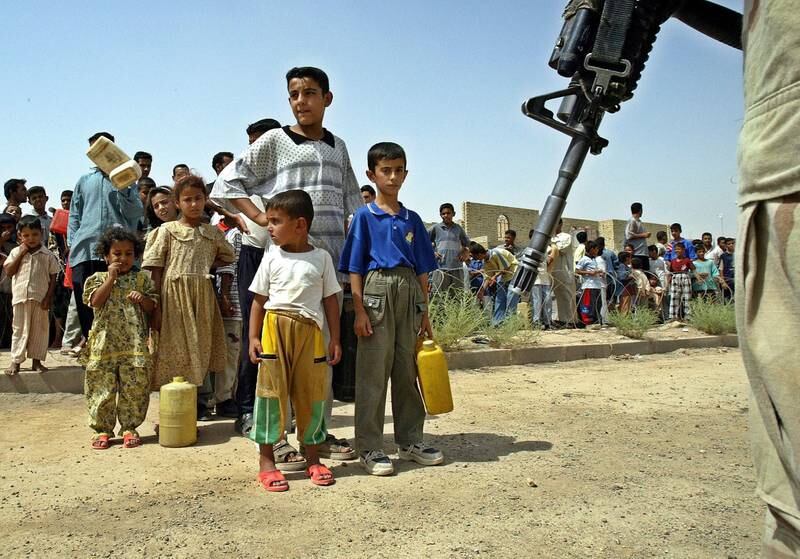 A US soldier stands guard in front of Iraqi children waiting to get petrol in Fallujah. EPA.