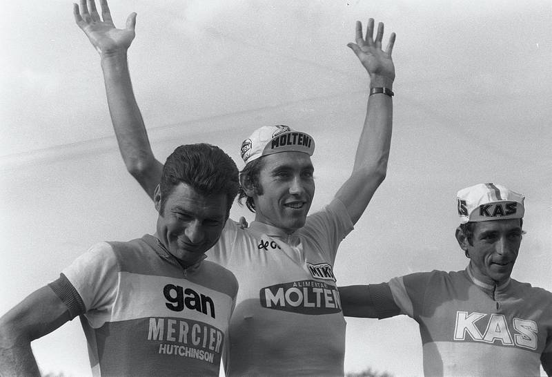 Belgian Eddy Merckx (C) smiles on the podium as he waves to the crowd 21 July 1974 in Paris after winning his fifth Tour de France (1969-1972, 1974) in front of Raymond Poulidor (L), who finished second at the age of 38 and Lopez-Carril of Spain. (Photo by STAFF and - / AFP)