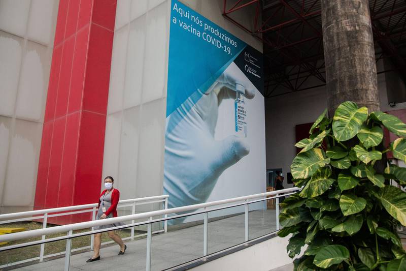 A worker in Rio de Janeiro  passes in front of a sign at a Fiocruz production facility that reads in Portuguese: "We produce the Covid-19 vaccine here." Brazil has administered 64 million Covid vaccine doses, with an average rate estimated at 659,189 doses per day. Bloomberg