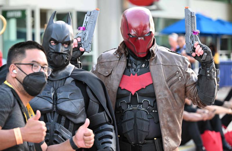 An attendee gets a photo with cosplayers dressed as Batman and Red Hood. AFP