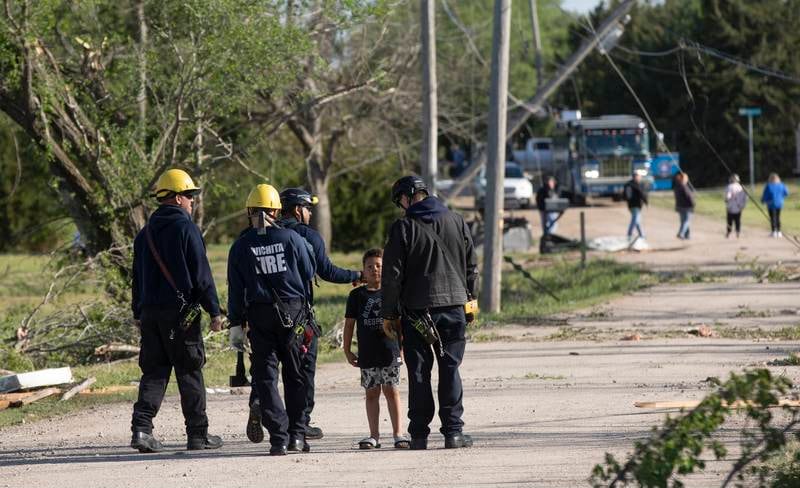 Camden Oyewole, 7, talks to firefighters searching an area in Andover after the tornado. AP