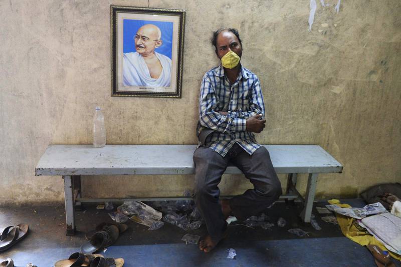TOPSHOT - A homeless man wearing a facemask sits beside a portrait Mahatma Gandhi at a shelter camp set up by Telangana state Government during a 21-day government-imposed nationwide lockdown as a preventive measure against the COVID-19 coronavirus, in Hyderabad on April 7, 2020. / AFP / NOAH SEELAM
