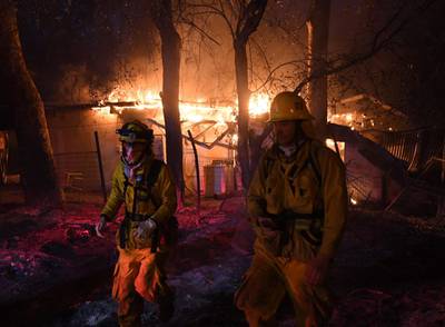 Firefighters move away from a burning house after discovering downed live power lines, as the Thomas wildfire continues to burn in Carpinteria, California. Mark Ralston / AFP