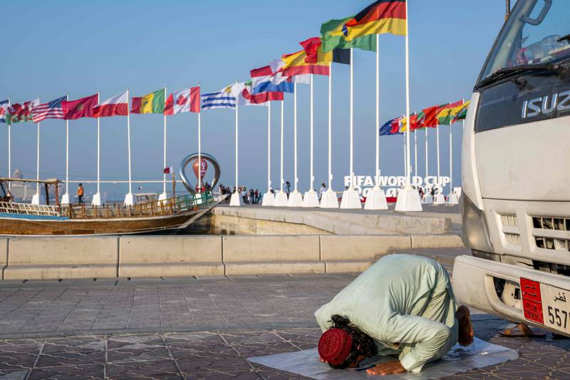 A worker prays near the flags of the World Cup participating countries in Doha.  AFP
