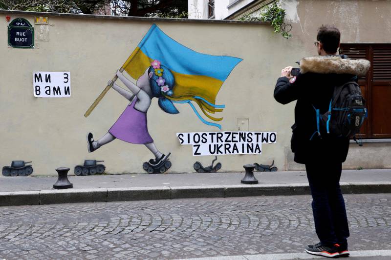 A man takes a picture of a fresco by street artist Seth globepainter depicting a girl with a Ukrainian flag walking on tanks in Paris. AFP