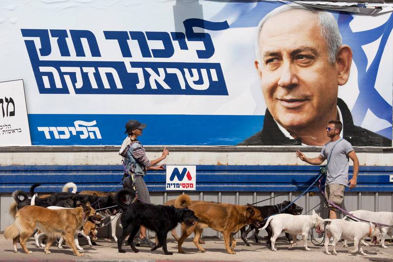 Dog walkers argue as they pass by an election campaign billboard shows Israeli Prime Minister Benjamin Netanyahu in Tel Aviv, Israel, Monday, April 8, 2019. Israel's election on Tuesday boils down to a referendum on Prime Minister Benjamin Netanyahu, who has dominated the country's politics for the better part of three decades. The Hebrew writing say "Strong Likud, Strong Israel. (AP Photo/Ariel Schalit)