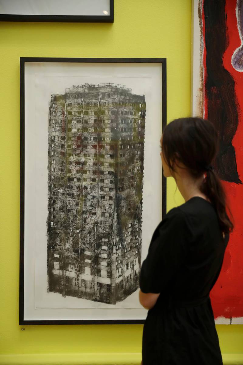 A woman poses for photographs in front of "Five Grand" by artist Luke Wade which shows the burnt out Grenfell Tower and features in this year's Summer Exhibition on it's 250th year at the Royal Academy of Arts in London, Tuesday, June 5, 2018. The Summer Exhibition has been held since 1769, with around 1300 works on display this year and most of them available for purchase. It runs from June 12 until August 19. (AP Photo/Matt Dunham)