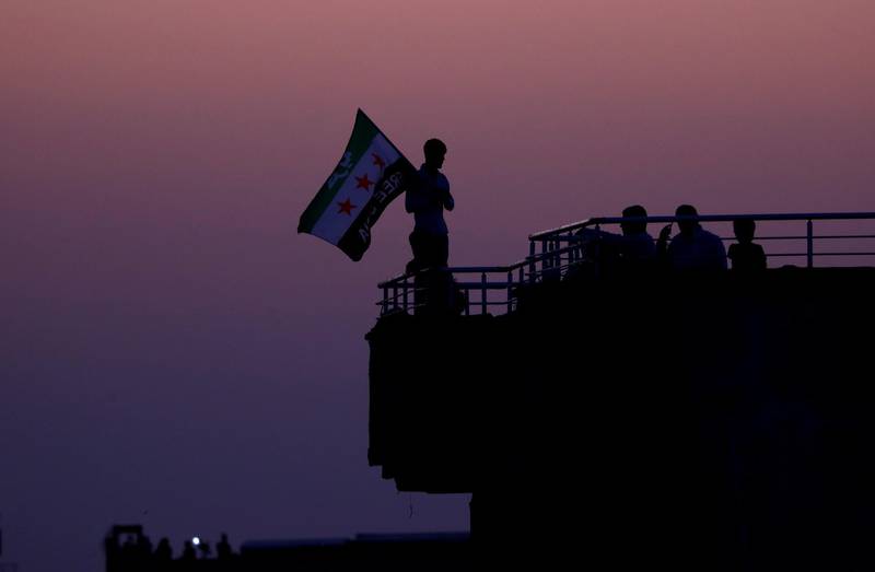 A man waves a Syrian opposition flag as he stands on top of an apartment building in the Turkish border town of Akcakale, in Sanliurfa province, Turkey. Reuters