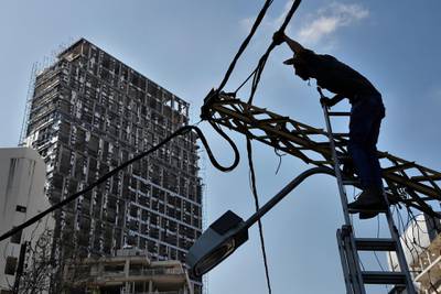 An electricity worker fixes power cables in front of a damaged building. AP Photo