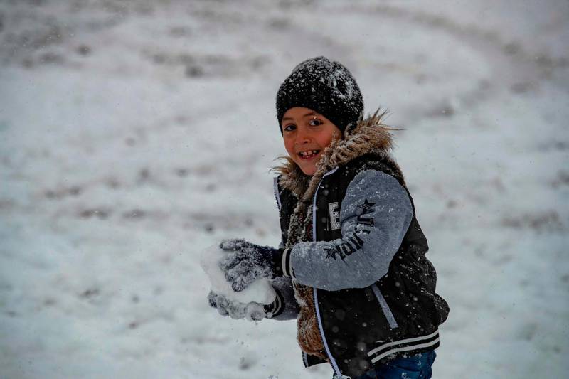 A boy holds a snowball as he stands in the snow in the northeastern Syrian town of Al Malikiyah at the border with Turkey after a blizzard.  AFP