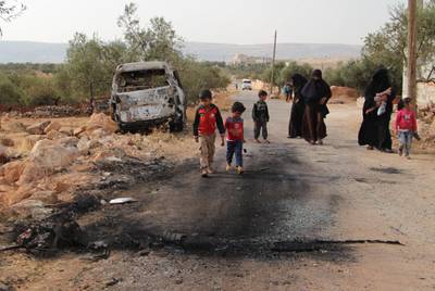 Syrian children walk past a damaged van at the site of helicopter gunfire which reportedly killed nine people near the north-western Syrian village of Barisha. AFP
