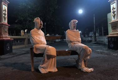 Volunteers Deri Setyawan and Septian Febriyanto sit on a bench as they play the role of 'pocong', or 'shroud ghost', to make people stay at home amid the spread of coronavirus disease. Reuters