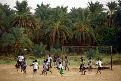 Youths play football near a date palm plantation in Barkal