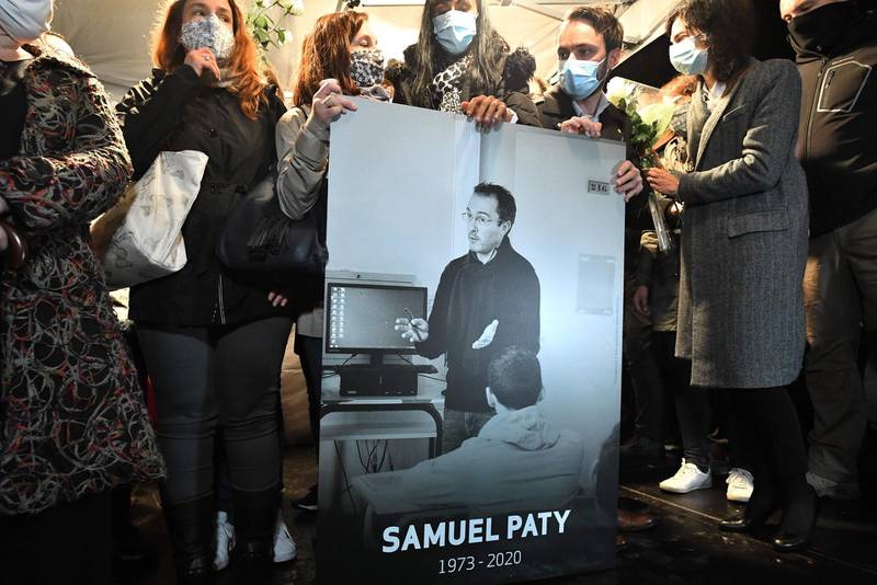 TOPSHOT - Relatives and colleagues hold a picture of Samuel Paty during the 'Marche Blanche' in Conflans-Sainte-Honorine, northwest of Paris, on October 20, 2020, in solidarity after a teacher was beheaded for showing pupils cartoons of the Prophet Mohammed. His murder in a Paris suburb on October 16 shocked the country and brought back memories of a wave of Islamist violence in 2015. Paty, 47, was attacked on October 16 on his way home from the junior high school where he taught by 18-year-old Chechen man Abdullakh Anzorov, who was shot dead by police. Following the attack, tens of thousands of people took part in rallies countrywide to honour Paty and defend freedom of expression. / AFP / Bertrand GUAY
