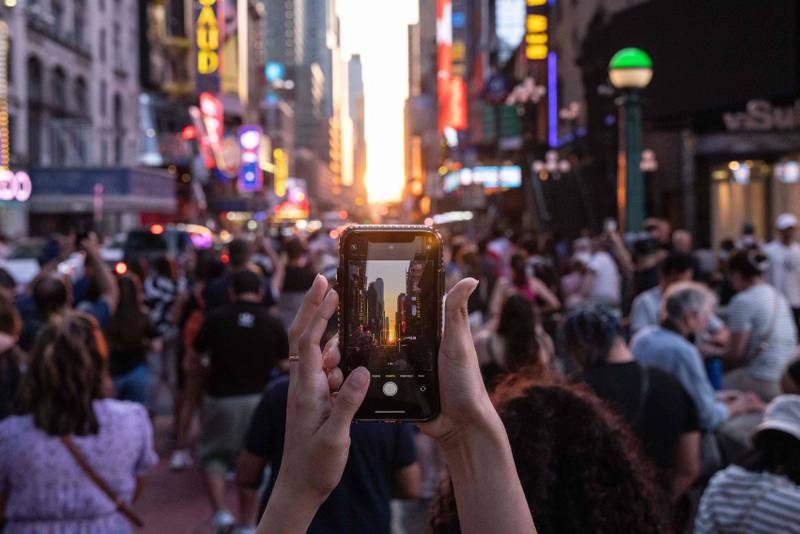 People take pictures as the sun sets over Manhattan on 42nd Street during Manhattanhenge in New York on Memorial Day 2022.  AFP