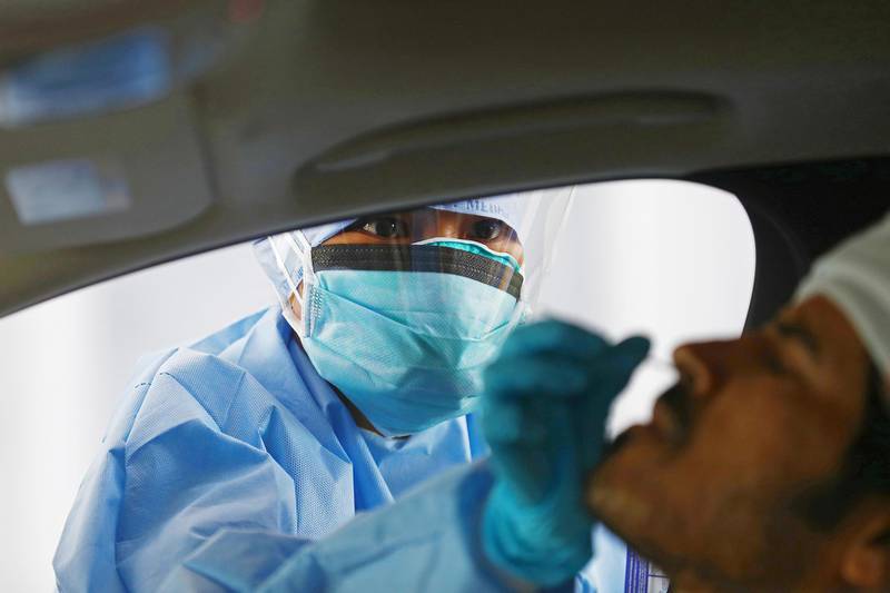 A health worker wearing protective clothing administers a swab test.