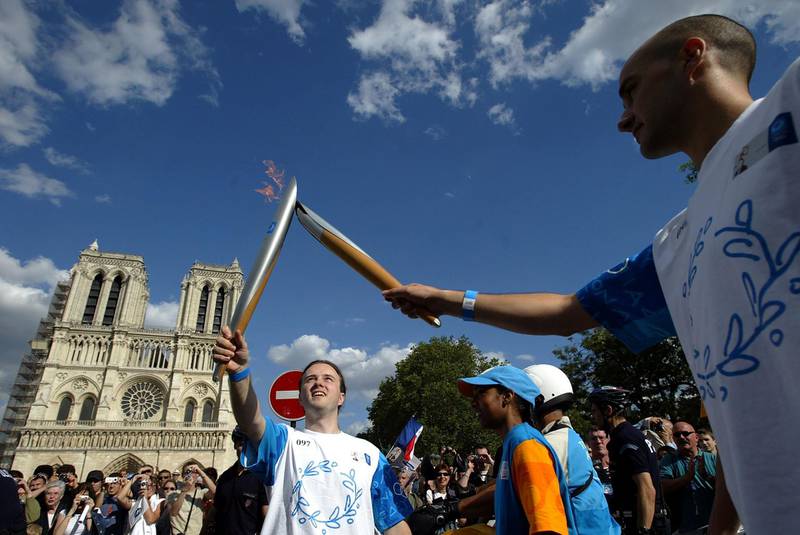 PARIS - JUNE 25:  Torchbearer Jerome Leydier (right) passes the Olympic Flame to Christophe Ottobrini (left) in front of the Notre Dame Cathedral during Day 21 of the Athens 2004 Olympic Torch Relay on June 25, 2004 in Paris, France. The Olympic Flame travels to 34 cities in 27 countries en route to the Athens 2004 Olympic Games.  (Photo by Todd Warshaw/Getty Images)