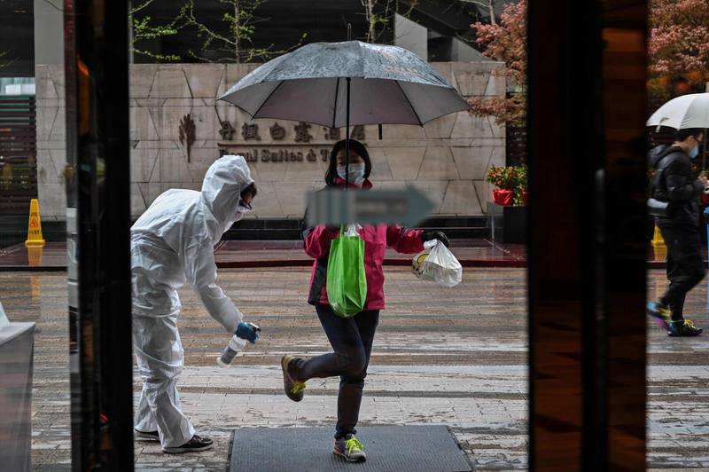 A hotel employee wearing a protective suit sprays disinfectant on an arriving guest, as a preventative measure against the COVID-19 coronavirus in Wuhan, China's central Hubei province, a day after travel restrictions into the city were eased following the outbreak. AFP