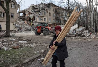 A woman carries wooden planks as she walks past a heavily damaged residential building following a Russian strike in the Donetsk region. AFP